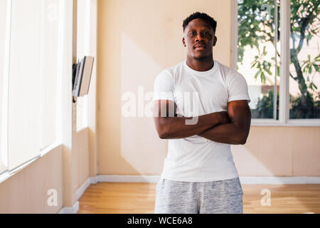 Montare fiducioso African American uomo in bianco t shirt in piedi con le braccia conserte e guardando la fotocamera in palestra sulla giornata di sole Foto Stock