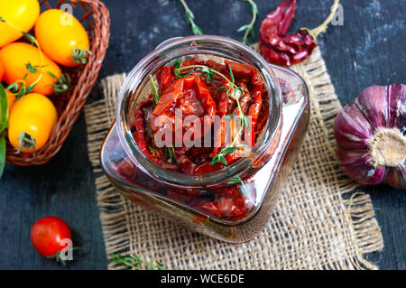 Pomodori secchi con erbe aromatiche, aglio in olio di oliva in un vasetto di vetro. Vista superiore, laici piatta Foto Stock