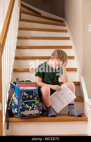 Disppointed boy, 8 anni, a casa con la sua scuola primaria relazione. Foto Stock