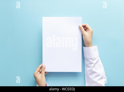 Close up mani tenendo vuoto vuoto bianco lettera di carta di formato A4 per il flyer o invito mock up isolata su uno sfondo blu. Foto Stock