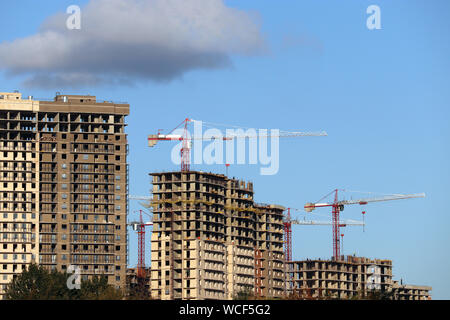 Gru edili e incompiuta di alto-aumento edifici residenziali sullo sfondo del cielo blu con nuvole Foto Stock