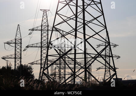 Impianto di alimentazione, linee di trasmissione di energia elettrica. Sagome di alta tensione torri con fili elettrici su sfondo al tramonto Foto Stock