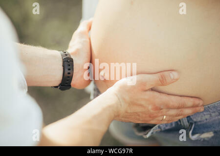 Un uomo tocca e abbraccia il ventre di sua moglie incinta durante la camminata. Primo piano. Foto Stock