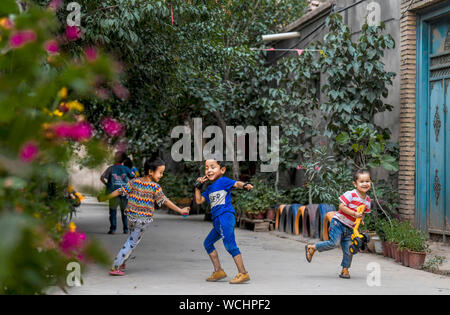 (190828) -- KASHGAR, Agosto 28, 2019 (Xinhua) -- i bambini si divertono in un vicolo a Qianjin Village a Kashgar, a nord-ovest della Cina di Xinjiang Uygur Regione autonoma, Agosto 18, 2019. Abitazioni circondato da fragranti sbocciano i fiori a profusione e ben disposte le case e i vicoli di un aspetto più ordinato, varie rivestimento alberi lungo le strade dove i bambini si divertono, la scena pastorale può essere visto ovunque nel villaggio di Qianjin. La bellezza idilliaca nel villaggio di Qianjin deriva dalla sua fiorente economia di fiori in cui Salima Sultan è un pioniere. Salima, un 60-anno-vecchio abitante, sviluppato la predilezione di f Foto Stock