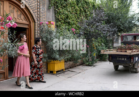 (190828) -- KASHGAR, Agosto 28, 2019 (Xinhua) -- Salima Sultan (R) e sua figlia Mihrigvl Rixat vedere un fiorista in fuori davanti a casa loro a Qianjin Village a Kashgar, a nord-ovest della Cina di Xinjiang Uygur Regione autonoma, Agosto 18, 2019. Abitazioni circondato da fragranti sbocciano i fiori a profusione e ben disposte le case e i vicoli di un aspetto più ordinato, varie rivestimento alberi lungo le strade dove i bambini si divertono, la scena pastorale può essere visto ovunque nel villaggio di Qianjin. La bellezza idilliaca nel villaggio di Qianjin deriva dalla sua fiorente economia di fiori in cui Salima Sultan è un pioniere. Foto Stock