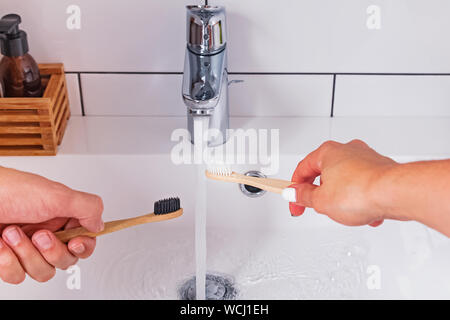 Uomo e donna di mani di close-up tenendo un bambù spazzolini da denti vicino al rubinetto di acqua in bagno moderno Foto Stock