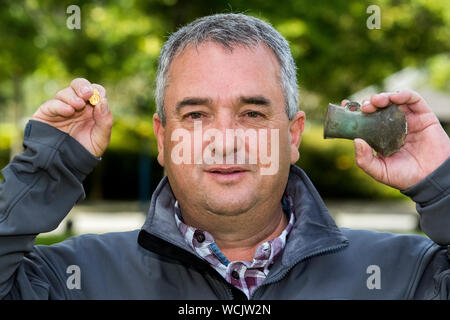 Il cacciatore di tesori Adrian McStraw tenendo premuto uno dei due età del bronzo tardo assi montati su zoccolo ha trovato in Aghadrumglasny, vicino Aghagallon, Co. Antrim datata 950-700 A.C. e un oro medievale di guarnizione dal Derrvullan, vicino a Enniskillen, Co. Fermanagh (XVII secolo) trovata vicino a Derryvullan chiesa e cimitero, vicino al sito di San Patrizio e. Foto Stock