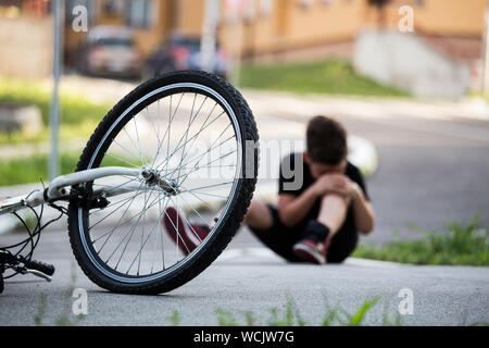 Ragazzo in via terra con un infortunio al ginocchio urlando dopo la caduta alla sua bicicletta Foto Stock