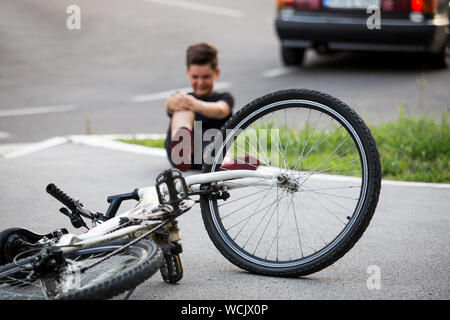 Ragazzo adolescente vi è un infortunio al ginocchio, come la bicicletta cade durante la guida. Kid male la gamba dopo la caduta dalla sua bici Foto Stock