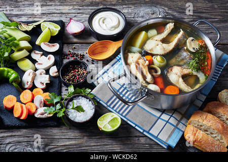 Piccanti trote zuppa di pesce con verdure e funghi in una pentola su una tavola di legno tavolo rustico con ingredienti, orizzontale vista da sopra Foto Stock