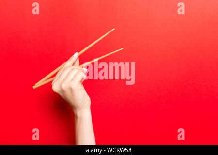 Immagine creativa delle bacchette di legno nelle femmine di mano su sfondo rosso. Il giapponese e il cinese del cibo con copia spazio. Foto Stock