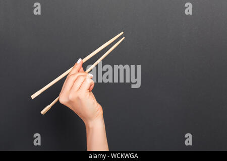 Immagine creativa delle bacchette di legno nelle femmine di mano su sfondo nero. Il giapponese e il cinese del cibo con copia spazio. Foto Stock