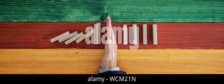 Ampia vista immagine di imprenditore di arresto a mano dei dominos da collassare in una immagine concettuale. Su sfondo colorato di tavole di legno. Foto Stock