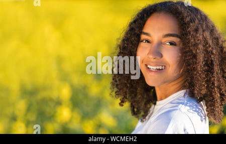 Bellissima gara di misto biracial americano africano ragazza adolescente femmine giovane donna sorridente e felice in un campo di fiori gialli Foto Stock