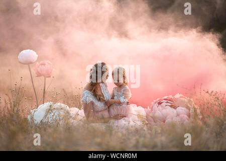 Mamma e figlia in rosa fiaba vestiti sono seduti in un campo circondato da grandi rosa fiori decorativi. Foto Stock