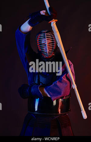 Immagine ravvicinata, Kendo fighter indossa in una corazza, tradizionale kimono, casco la pratica delle arti marziali con shinai spada di bambù, sfondo nero. Foto Stock