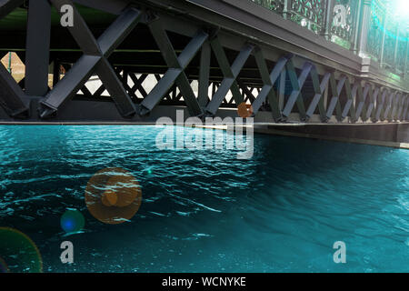 Ponte attraverso il canale dell'acqua. Telaio in metallo struttura oltre il puro fiume calmo. Moderna città urbana paesaggio con vista prospettica nella giornata di sole Foto Stock