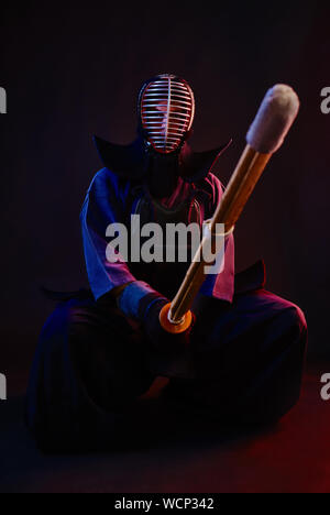 Close up. Combattente di Kendo di indossare in una corazza, tradizionale kimono, casco, seduto, praticanti di arti marziali con shinai spada di bambù, sfondo nero. Foto Stock