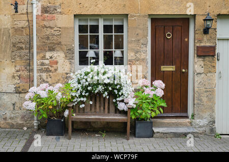 Panca in legno e fiori nella parte anteriore di un cotswold cottage in pietra. Chipping Campden, Cotswolds, Gloucestershire, Inghilterra Foto Stock