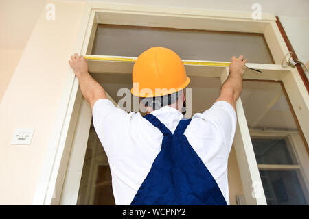 Operaio edile tuttofare e sta lavorando alla ristrutturazione dell appartamento. Builder è la misurazione della porta della camera utilizzando una misura nastro nel sito in costruzione. Foto Stock