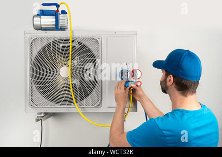 Servizio di installazione di fissare la riparazione manutenzione di un condizionatore di aria unità esterna, da cryogenist tecnico lavoratore evacuare il sistema con pompa per vuoto a Foto Stock