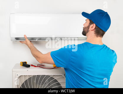 Servizio di installazione di fissare la riparazione manutenzione di un condizionatore di aria unità interna, da cryogenist tecnico lavoratore in maglietta blu e berretto da baseball Foto Stock