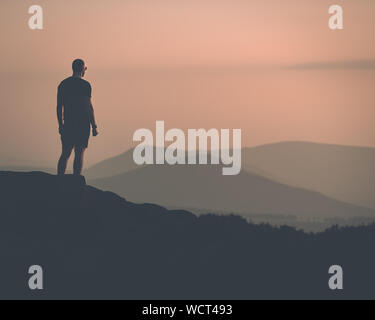 Fiducioso giovane maschio muscolare si presentò con una silhouette di montagne in distanza Foto Stock