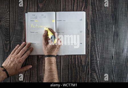 Appartamento laico mani del marcatore di contenimento in prossimità di aprire il calendario in bianco su marrone pulito tavolo in legno, vista da sopra. Foto Stock