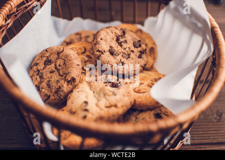 Biscotti al cioccolato risiede in un cesto di vimini. Un cestello con senza glutine i cookie su un tavolo di legno. Messa a fuoco selettiva. Foto Stock