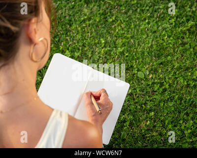 Close-up di imprenditrice seduta in erba verde e la scrittura di pianificazione nel diario del calendario Foto Stock