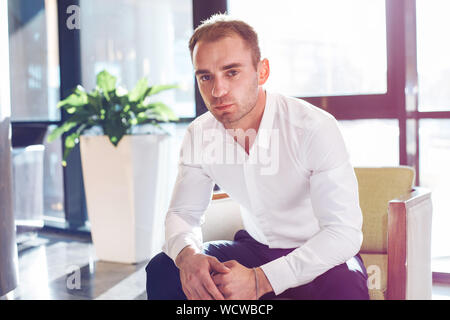 Grave Uomo in camicia bianca seduto in poltrona in ufficio contemporaneo Foto Stock