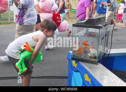 Ragazzo con animali impagliati nascosto sotto il suo braccio guardando il pesciolino che vengono fornite come un premio presso la locale fiera agricola Foto Stock