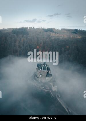 Immagine aerea verticale del castello di Eltz circondato da nuvole E alberi in Germania Foto Stock