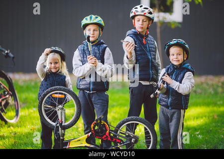 Bambini meccanica, riparazione di biciclette. Contenti i bambini che fissa bike insieme all'aperto nella giornata di sole. Riparazione di biciclette concept. Il lavoro di squadra famiglia in posa con strumenti Foto Stock