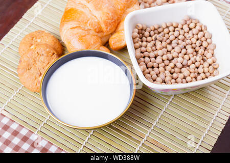 Il latte nella ciotola con croissant pane cotto, soia nella tazza in legno di bambù e di copiare lo spazio per testo. vista superiore Foto Stock