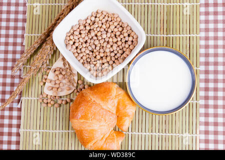 Croissant pane cotto con il latte nella tazza di fagioli di soia in tazza di cookie e spezie in legno di bambù. copia spazio per testo. vista superiore Foto Stock