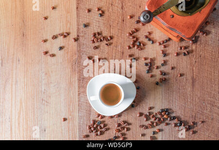Vista dall'alto di un espresso servito in una tazza bianca circondata da chicchi di caffè tostati e un piccolo mulino su un tavolo di legno. Foto Stock