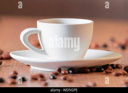Una tazza bianca con una messa a fuoco selettiva circondata da grandi chicchi di caffè tostati su un tavolo di legno. Foto Stock