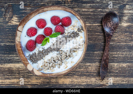 Frullato di cocco in ciotola con lamponi, fiocchi d'avena, semi di girasole e semi di Chia per la prima colazione , vicino. Il concetto di mangiare sano, super. Foto Stock