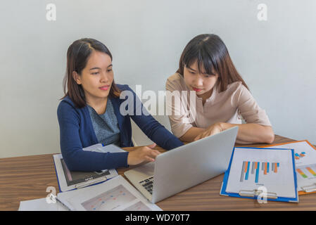 Giovani femmine di advisor finanziario lavorando su laptop e statistiche paperworks Foto Stock