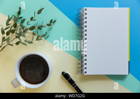 Blank notebook, caffè, ramo di eucalipto e penna su carta pastello sfondo. Business start-up e torna al concetto di scuole Foto Stock