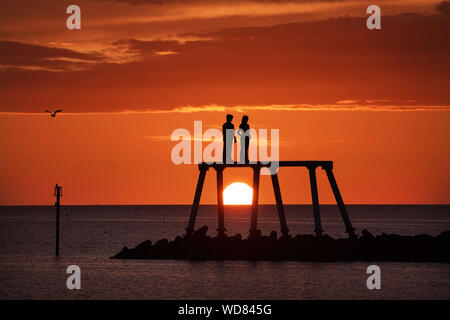 Il sole sorge sulla scultura " La Coppia " da artista Sean Henry, a Newbiggin-per-il-mare in Northumberland. Foto Stock