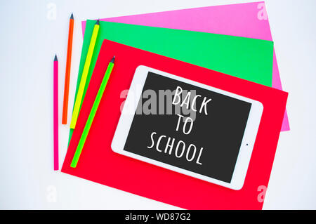 Carta colorata, neon matite e tablet su sfondo bianco con copyspace. Piatto stile di laici. Si torna a scuola concetto. Foto Stock