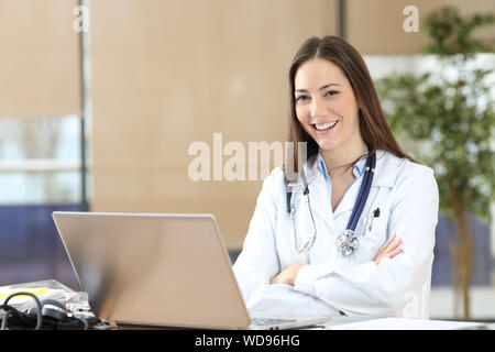 Felice medico donna in posa guardando la telecamera seduto alla consultazione Foto Stock