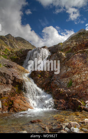 Una piccola cascata su red color rocce e massi, spruzzi in un piccolo lago Foto Stock