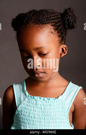 Triste African bambina isolata su uno sfondo nero con un vestito blu a. Foto Stock