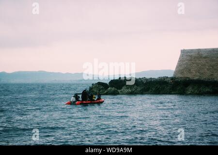 Ampio colpo di persone in una barca gonfiabile sul corpo d'acqua vicino ad una piccola scogliera Foto Stock