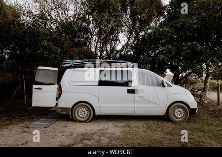 Foto ravvicinata di un pulmino bianco parcheggiato vicino agli alberi Foto Stock