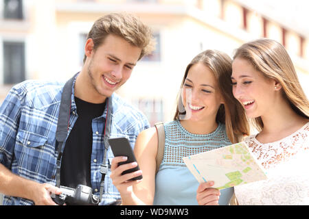 Tre felici turisti in viaggio controllo smart phone gps e la mappa nella strada sulla vacanza estiva Foto Stock