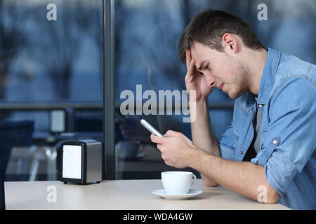Vista laterale verticale di un triste uomo controllo cellulare telefono messaggio in un coffee shop Foto Stock